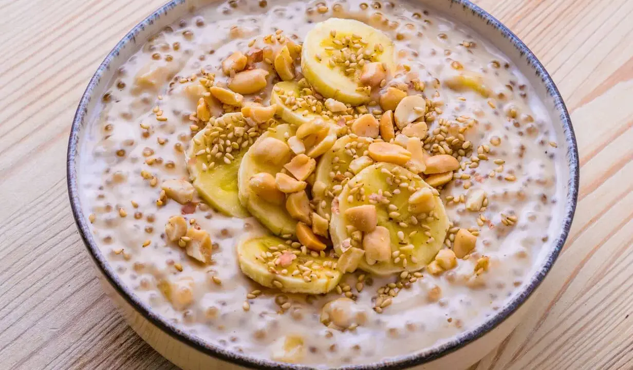 Schüssel mit cremigem vietnamesischem Dessert, garniert mit Bananenscheiben, Erdnüssen und Sesam.