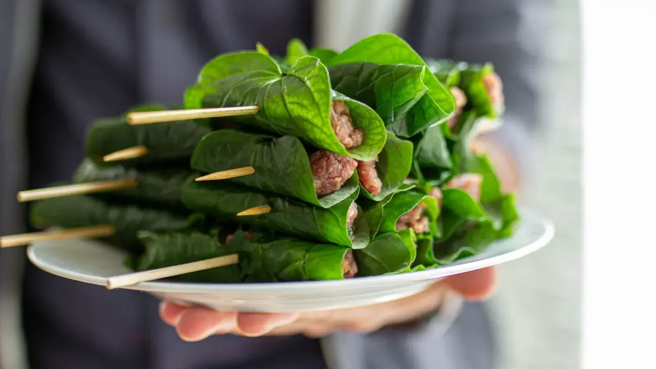 Bo la lot, ein vietnamesisches Gericht, auf einem Teller präsentiert. Fleisch ist in grüne Blätter gewickelt und mit Holzspießen fixiert.