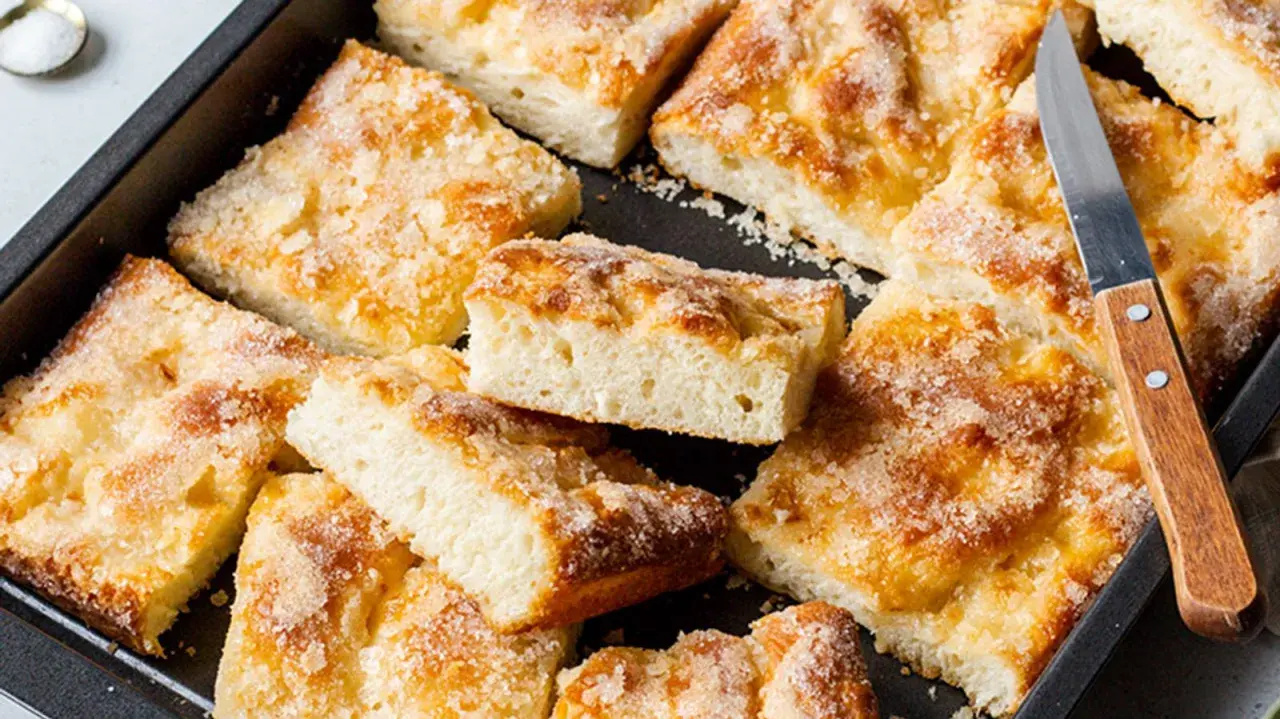 Ein Blech mit saftigem, **schneller Butter zuckerkuchen**, in Stücke geschnitten. Ein Messer liegt bereit.