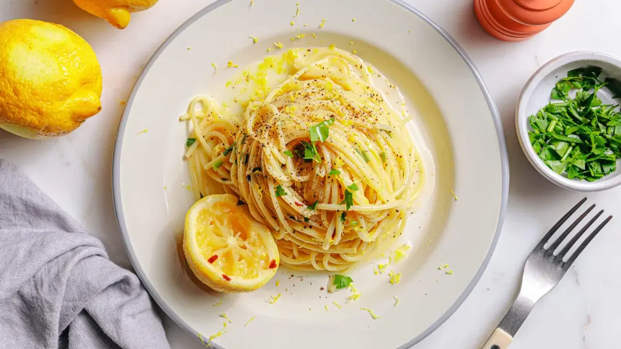 Vegane Pasta mit Zitronenschale und Kräutern, garniert mit einer Zitronenhälfte und frisch gemahlenem Pfeffer.