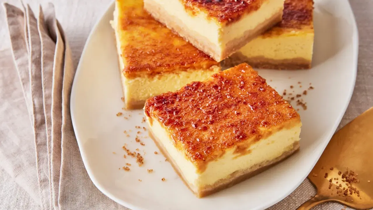 Köstliche Stücke Creme Brulee Kuchen mit karamellisierter Zuckerkruste auf einem Teller, daneben eine goldene Tortenheber.