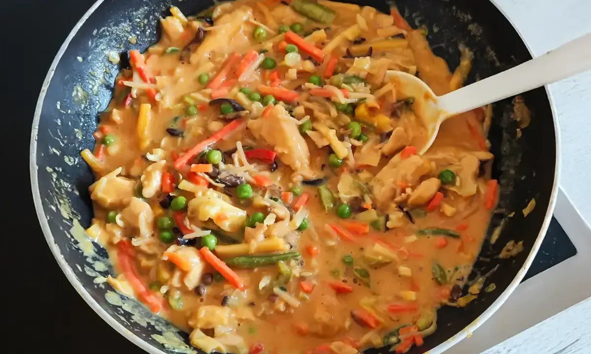 Ein köstliches veganes Curry mit viel Gemüse wie Karotten, Erbsen und Bambussprossen wird in einer Pfanne zubereitet.