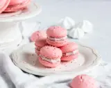 Rosa Macarons mit Himbeer-Ganache-Füllung, bestreut mit Zuckerperlen, auf einem Teller.