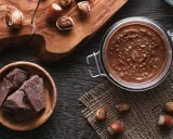 Zutaten für Nuss-Nougat-Creme selber machen: Haselnüsse, Schokolade und ein Glas voller Genuss.
