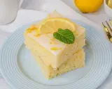 Zwei saftige Stücke weltbester Zitronenkuchen mit Joghurt, garniert mit Zitrone und Minze, auf einem blauen Teller.