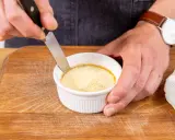 Ein Messer löst den Rand eines cremigen Flan Puddings in einer weißen Keramikschale.