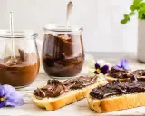 Zwei Gläser mit schoko creme, daneben Brotscheiben, üppig bestrichen mit der cremigen Schoko-Leckerei, verziert mit Veilchen.