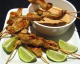 Saftige sate spiesse mit Erdnusssauce und Limettenspalten auf einem weißen Teller.