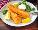 Zwei goldbraun frittierter Fisch mit Zitronenspalten, Sauce und Salat auf einem Teller.
