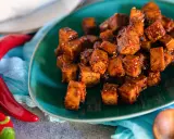 Würzig gebratene Tofuwürfel auf einem grünen Teller, daneben rote Chilis. So schmeckt Tofu!