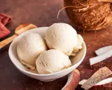 Cremiges Kokoseis selber machen mit Eismaschine: Drei Kugeln in einer Schale, daneben Kokosnussstücke und ein Löffel.