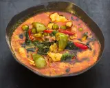 Ein dampfender rote thai curry mit Hühnchen, grünen Auberginen und roten Chilis in einer dunklen Schüssel.