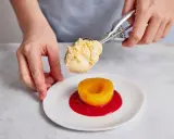 Eine Kugel Vanilleeis wird auf einen Pfirsich Melba mit Himbeersauce gegeben.
