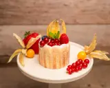 Ein kleiner Charlotte Kuchen, verziert mit frischen Beeren, Physalis und einem Hauch Puderzucker.