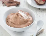 Cremige Schokoladen-Namelaka in einer Schüssel, daneben ein Löffel und Schokoladenstücke.