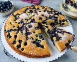 Saftiger Blaubeerkuchen, der nach viel Eiern schmeckt, mit Puderzucker bestäubt. Daneben eine Schüssel voller frischer Blaubeeren.