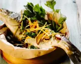 Gedämpfter Fisch, asiatisch zubereitet, mit Ingwer, Frühlingszwiebeln und frischen Kräutern in einem Bambuskorb.