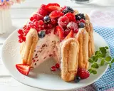 Eine köstliche Charlotte Torte, umhüllt von Löffelbiskuits und üppig belegt mit frischen Beeren wie Erdbeeren, Himbeeren und Johannisbeeren.