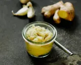 Frisch zubereitete ingwer knoblauch paste in einem Glas, daneben Ingwerwurzel und Knoblauchzehen auf dunklem Untergrund.