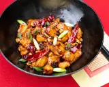 Ein köstliches Gericht mit asiatischen Rezepten mit Huhn, garniert mit Chilis und Frühlingszwiebeln in einer schwarzen Schüssel.