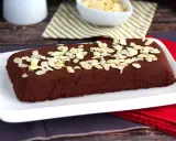 Dunkle, rechteckige marquise au chocolat, bestreut mit Mandelblättchen, auf einem weißen Teller.