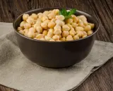 Schüssel mit Kichererbsen, die auf einem Leinentuch auf Holzhintergrund steht. Keine Sorge, Kichererbsen aus der Dose sind nicht giftig!