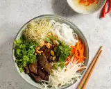 Bun bo nam bo: Reisnudeln, Rindfleisch, Sprossen, Karotten, Kohl und Kräuter in einer Schüssel, garniert mit Erdnüssen.