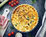 Herzhafte Quiche mit Speck und Lauch, perfekt für herzhafte Quiche Rezepte. Dazu frische Tomaten und Kräuter.