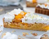 Ein Stück Mandarinen Tarte mit Baiserhaube, Mandelsplittern und frischer Zitronenschale bestreut.