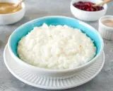 Cremiger Milchreis in einer blauen Schüssel, daneben Schüsseln mit Apfelmus, Kirschen und Zimt. Ein köstlicher Reis-Genuss.