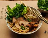 Cao Lau: Nudelschüssel mit Schweinefleisch, Sprossen und Kräutern, garniert mit knusprigen Krusten. Goldene Stäbchen ruhen auf dem Gericht.