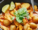 Ein köstliches Massaman Curry Rezept mit Hühnchen, Kartoffeln und Erdnüssen, garniert mit frischen Kräutern und Limettenspalten.