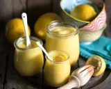 Leichte Zitronencreme im Thermomix zubereitet, serviert in Gläsern mit Löffeln, daneben frische Zitronen und ein Zitruspresse.
