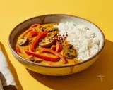 Schüssel mit Reis und rotem Curry, das mit Paprika und Pilzen verfeinert ist. Ein Hauch von Chiliflocken deutet an, dass dieses rote Curry scharf ist.