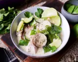 Ein cremiger Thai Green Curry mit Hühnchen, Zucchini, Zuckerschoten und Auberginenscheiben, garniert mit Limettenspalten und Koriander.