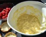 Frische Himbeeren warten neben leeren Tartelettförmchen und einer Schüssel mit cremiger Füllung auf die Fertigstellung der Himbeer Tartelettes.