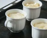 Vier weiße Förmchen mit luftiger Masse für ein Käsesoufflé stehen auf einem Backblech.