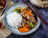 Reis mit einem herzhaften Stir-Fry-Gericht, das mit viel Gemüse und Fleisch in einer köstlichen Sauce serviert wird. Dazu gibt es eine kleine Schale mit scharfer Sauce.
