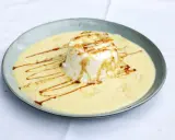 Ein leichtes, schwebendes Dessert aus Eischnee, umgeben von cremiger Vanillesauce, garniert mit Mandelsplittern und Karamell.