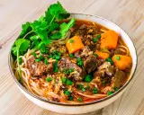 Herzhaftes Bo Kho mit zarten Rindfleischstücken, Karotten und Nudeln, garniert mit Koriander und Frühlingszwiebeln.