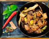 Ein dampfender Topf mit würzigem Beef Rendang, daneben frische Kaffirlimettenblätter, Chili und Gewürze.
