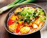 Herzhaftes Bun Rieu mit Tofu, Tomaten und frischen Kräutern, garniert mit Frühlingszwiebeln.