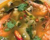 Eine dampfende Schüssel mit scharfer Thai Suppe, gefüllt mit Garnelen, Pilzen und Chili.
