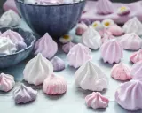 Zuckergebäck, was ist Meringue? Zarte, luftige Baisers in Rosa-, Lila- und Weißtönen, einige in einer Schüssel, andere verstreut.