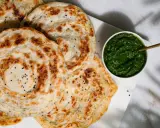 Fluffiger Roti Canai mit schwarzen Sesamkörnchen, daneben eine Schale mit grüner Chutney-Sauce.