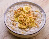 Schüssel mit cremigem vietnamesischem Dessert, garniert mit Bananenscheiben, Erdnüssen und Sesam.