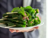 Bo la lot, ein vietnamesisches Gericht, auf einem Teller präsentiert. Fleisch ist in grüne Blätter gewickelt und mit Holzspießen fixiert.