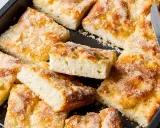 Ein Blech mit saftigem, **schneller Butter zuckerkuchen**, in Stücke geschnitten. Ein Messer liegt bereit.