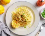 Vegane Pasta mit Zitronenschale und Kräutern, garniert mit einer Zitronenhälfte und frisch gemahlenem Pfeffer.