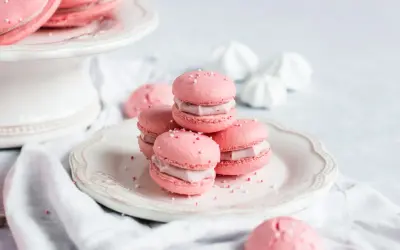 Rosa Macarons mit Himbeer-Ganache-Füllung, bestreut mit Zuckerperlen, auf einem Teller.